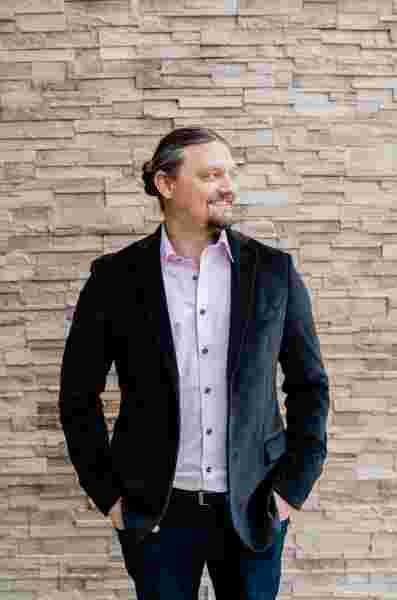 Matthew Young standing in front of a stone wall in a collard shirt and jacket
